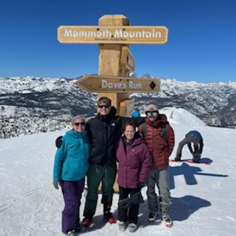 Four people on snowy mountain top pose in front of sign that reads Mammoth Mountain